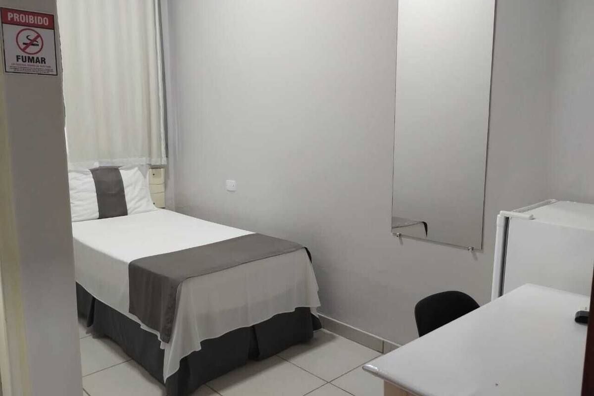 A small, clean room with a bed, a desk, and a mirror.