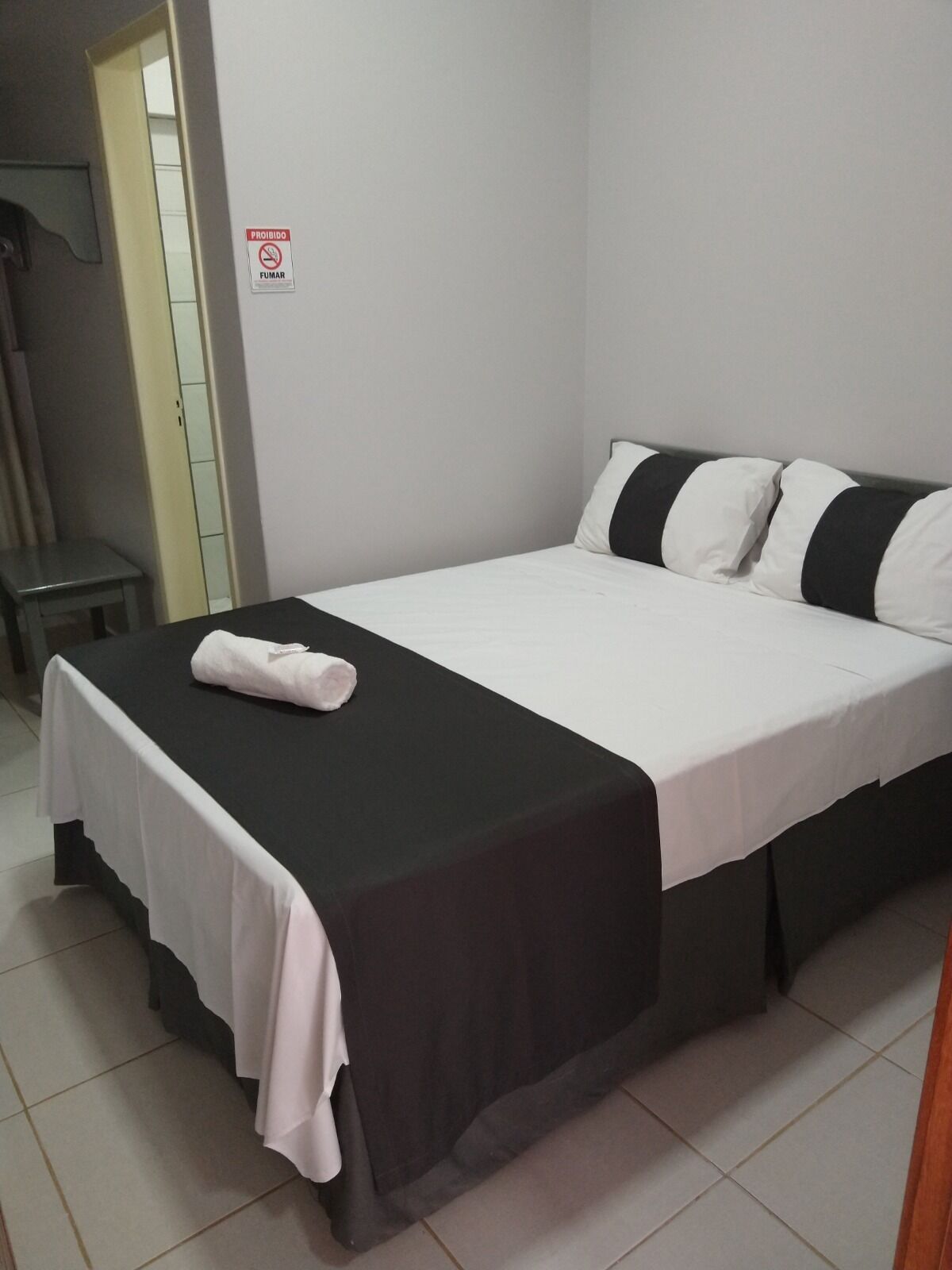 Een net opgemaakt bed met een zwart-wit gestreept kussen, een witte handdoek en een bordje met een rookverbod.