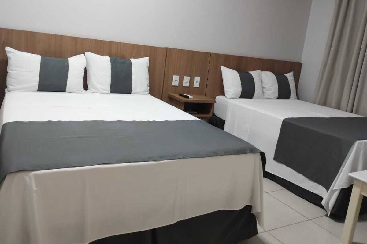 A hotel room with two beds, each with a grey and white bedspread, a wooden headboard, and a small bedside table with a lamp.
