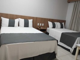 Habitación de hotel con dos camas, cada una con una colcha gris y blanca, un cabecero de madera y una mesita de noche con lámpara.