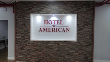 Letrero que dice 'Hotel American' con un fondo de pared de piedra.