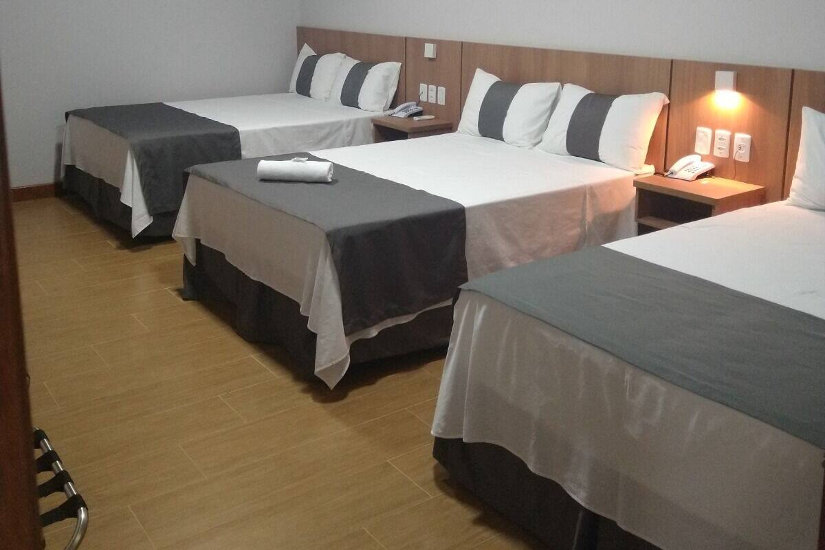 A hotel room with three single beds, each with a pillow and a small bedside table with a lamp.