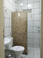 Baño con inodoro blanco, lavamanos y cabina de ducha con encimera de granito.