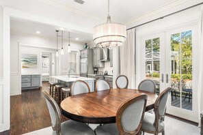 A dining room with a wooden table and chairs, a chandelier, and a view of the outdoors through a glass door.