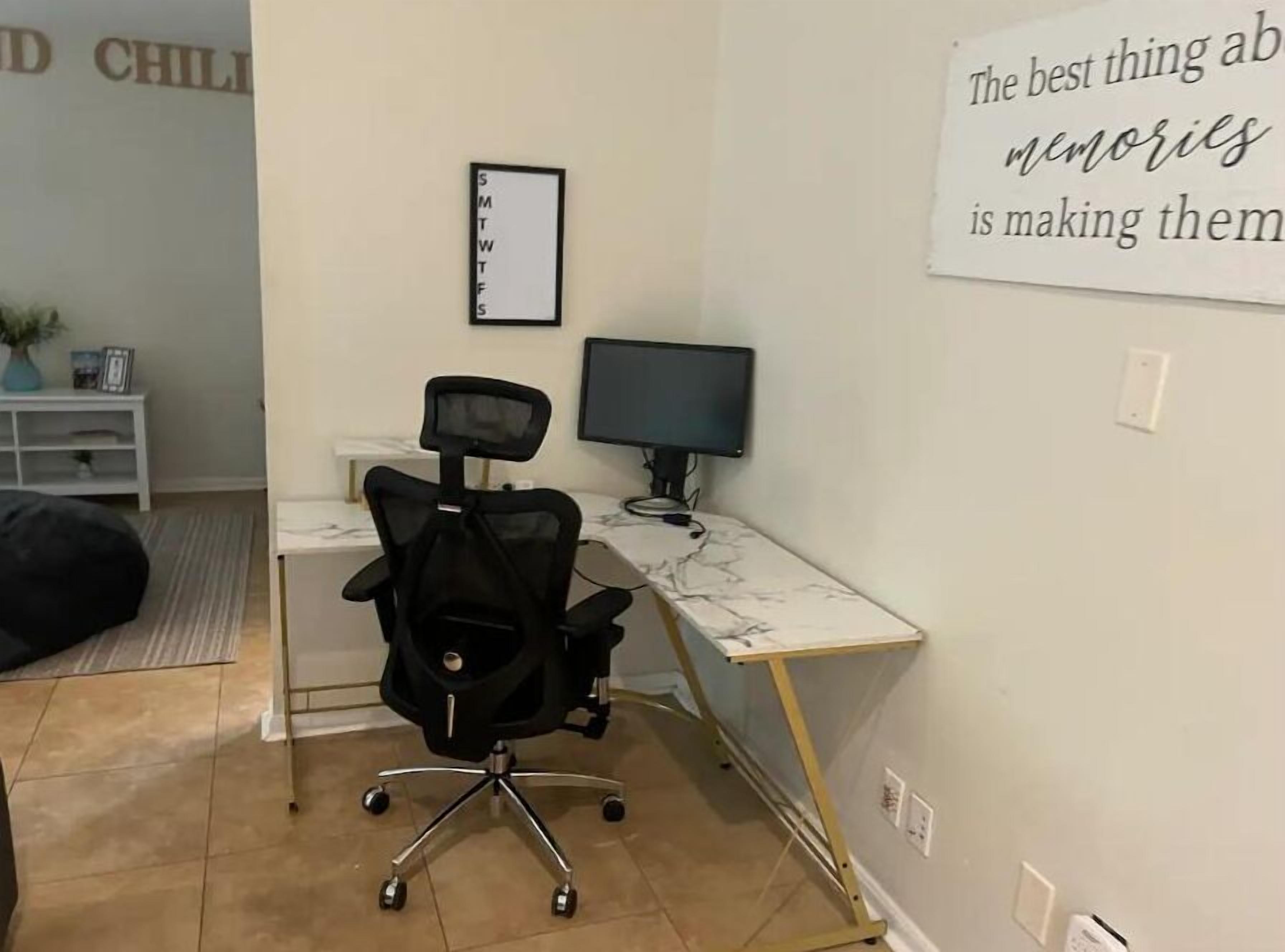 A home office with a desk, chair, computer, and a motivational quote on the wall.