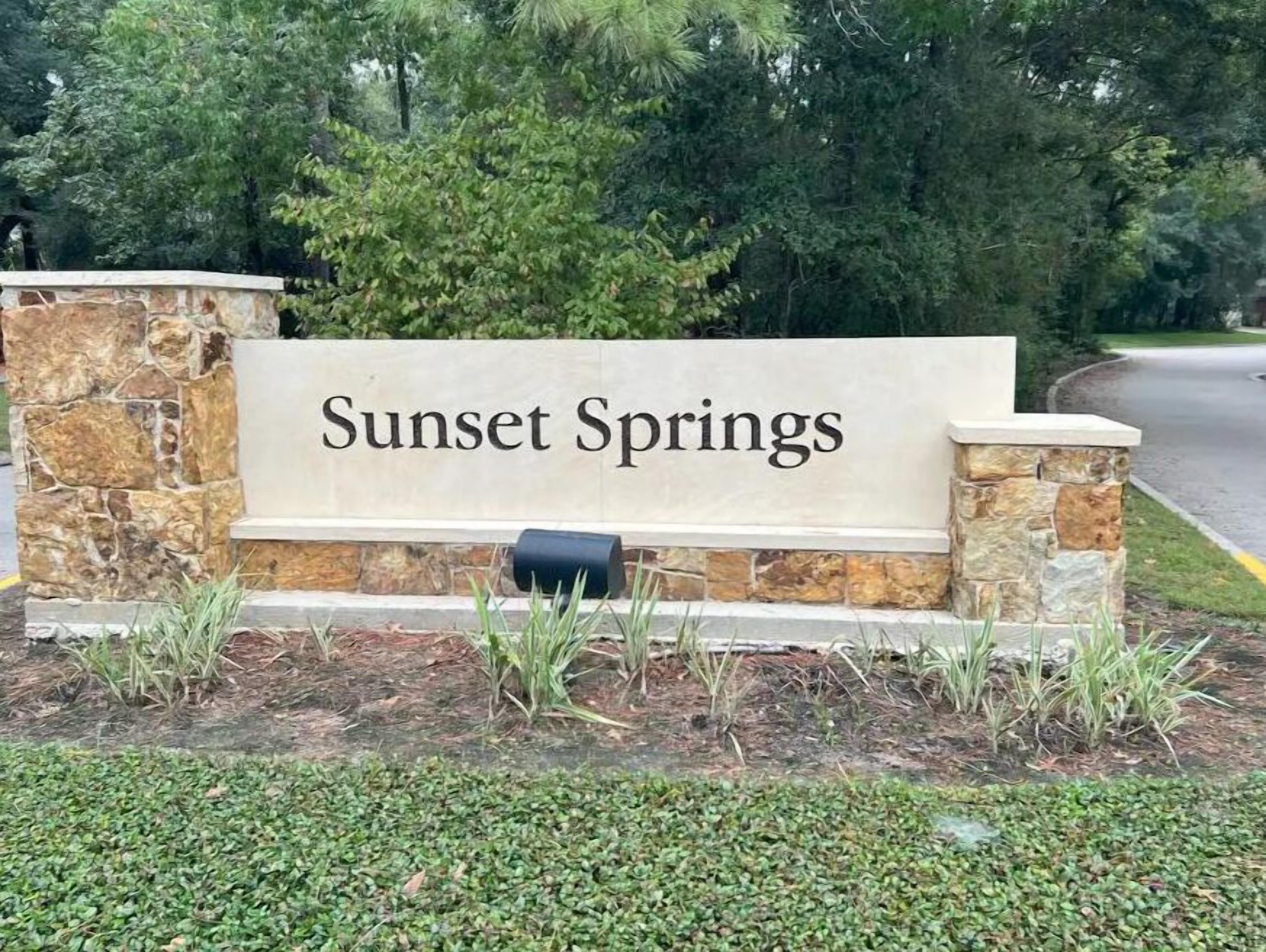 A stone sign with "Sunset Springs" written on it, surrounded by greenery and trees.