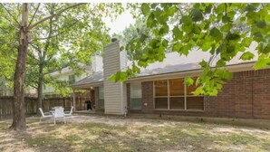 A backyard with a wooden deck, a brick house, and a tree.