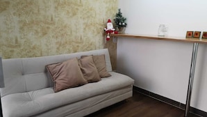 A living room with a grey sofa, a small Christmas tree, and a shelf with decorative items.