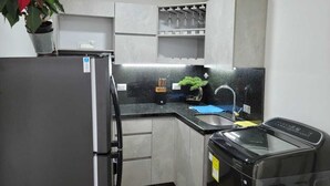 A compact kitchen with a refrigerator, sink, and dishwasher. There is a potted plant on the counter and a small shelf with glassware.