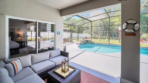 A covered patio area with a pool, a sofa, and a lantern. - EV_5334 - 4 Bed 3 Bath Home with Screened-in Pool, Games Room, Kids Bedrooms (Kissimeee)