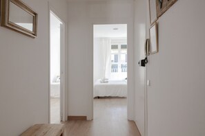 Un couloir mène à une chambre où se trouvent un lit, un banc en bois et un miroir accroché au mur.