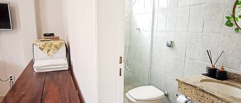 A bathroom with a wooden bench, a toilet, a shower, and a sink with a plant.