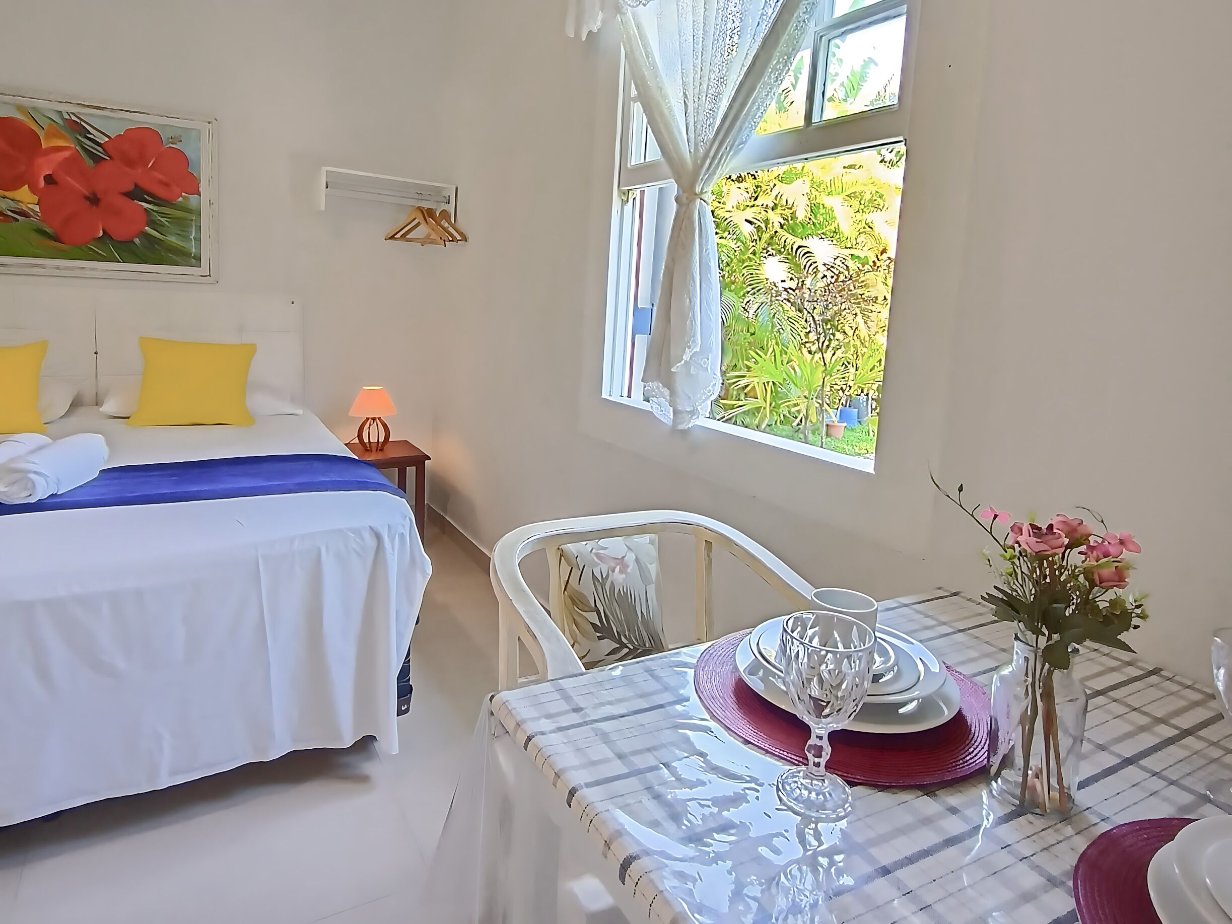 A hotel room with a bed, a table with a glass, and a window with curtains.