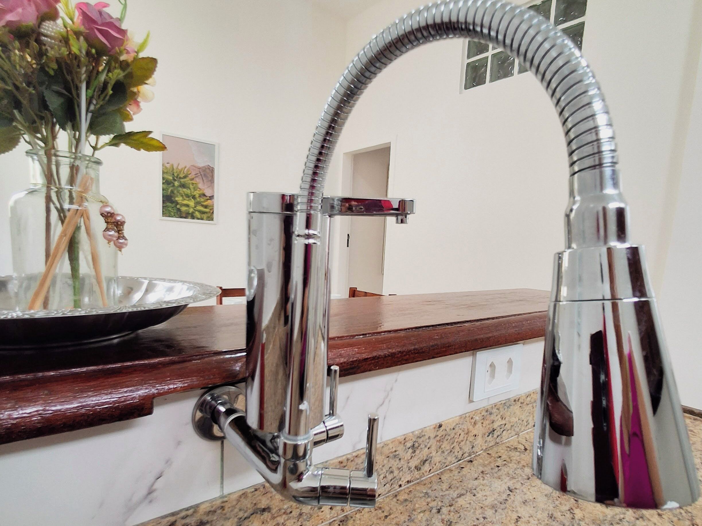 A kitchen with a stainless steel faucet, a marble countertop, and a vase with flowers on the counter.