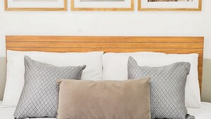 Un lit avec une tête de lit en bois, trois oreillers et trois tableaux encadrés accrochés au mur.