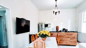 Une cuisine moderne dotée d’un îlot central, d’un coin repas avec des chaises et une table en bois, et d’un téléviseur fixé au mur.