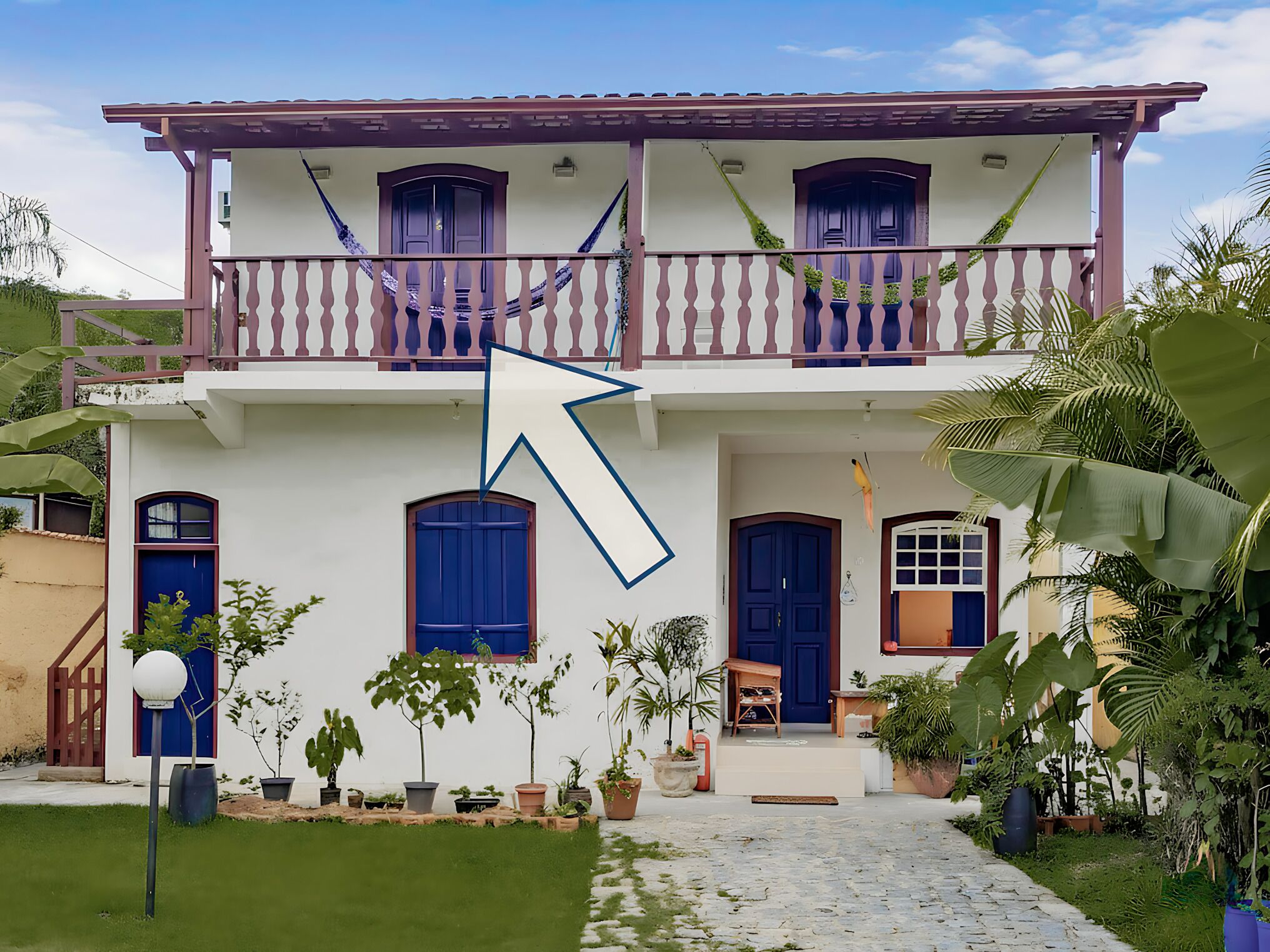 A two-story building with a balcony, potted plants, and a stone pathway leading to the entrance.