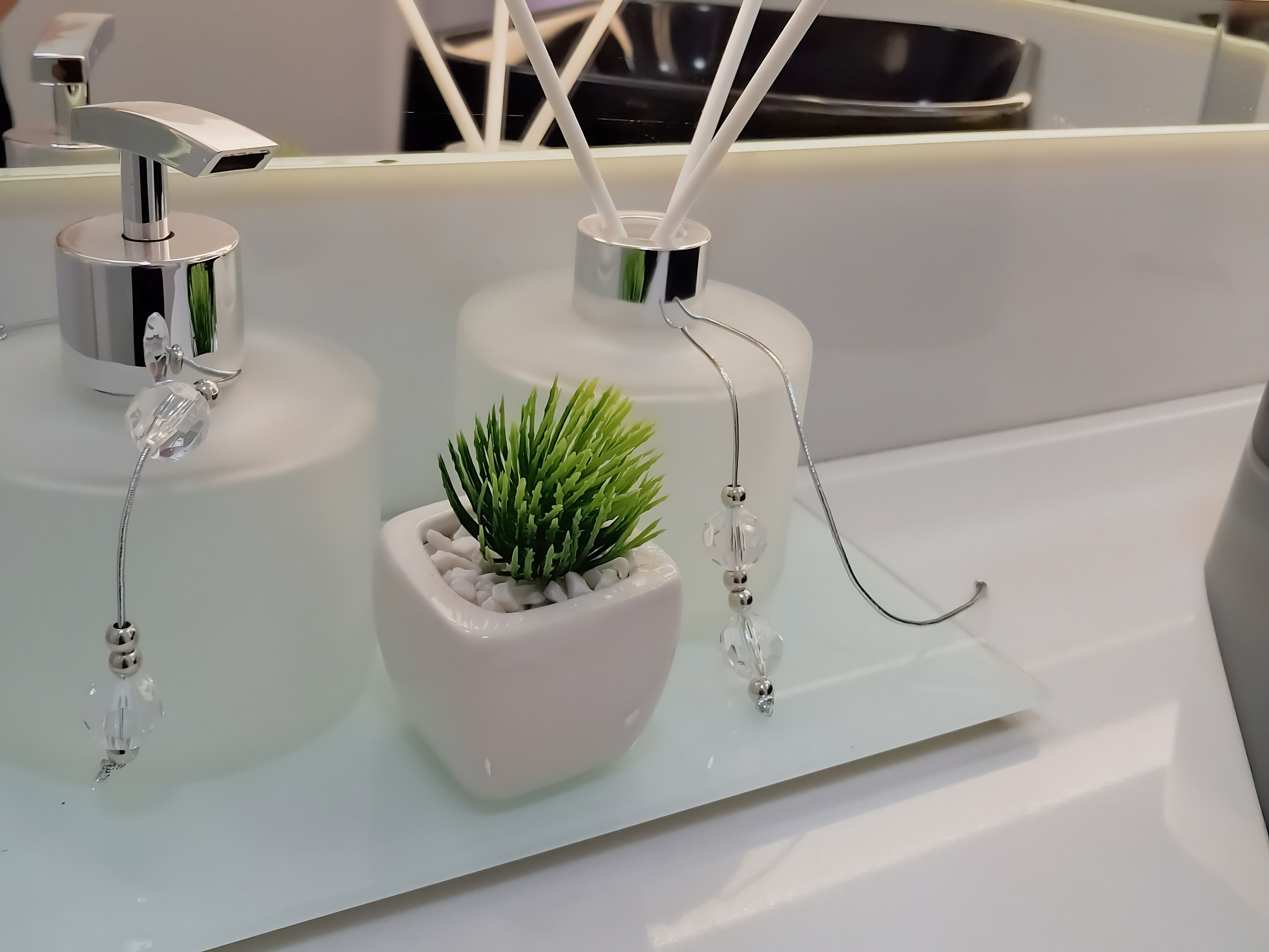 A bathroom sink with a small potted plant, a mirror, and two soap dispensers.