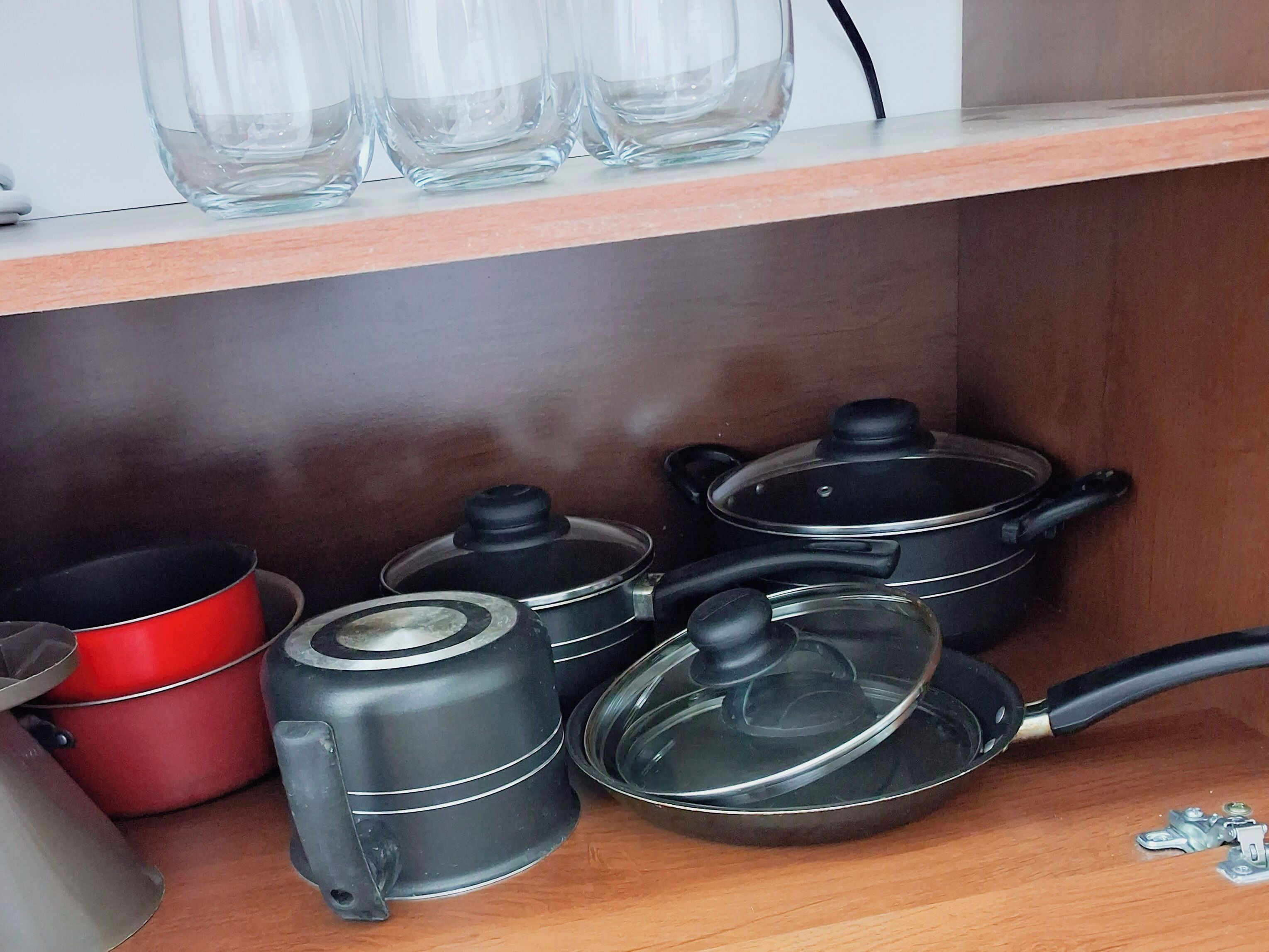 A kitchen with a wooden shelf holding clear glass bottles, a red pot, and several black pots with lids.