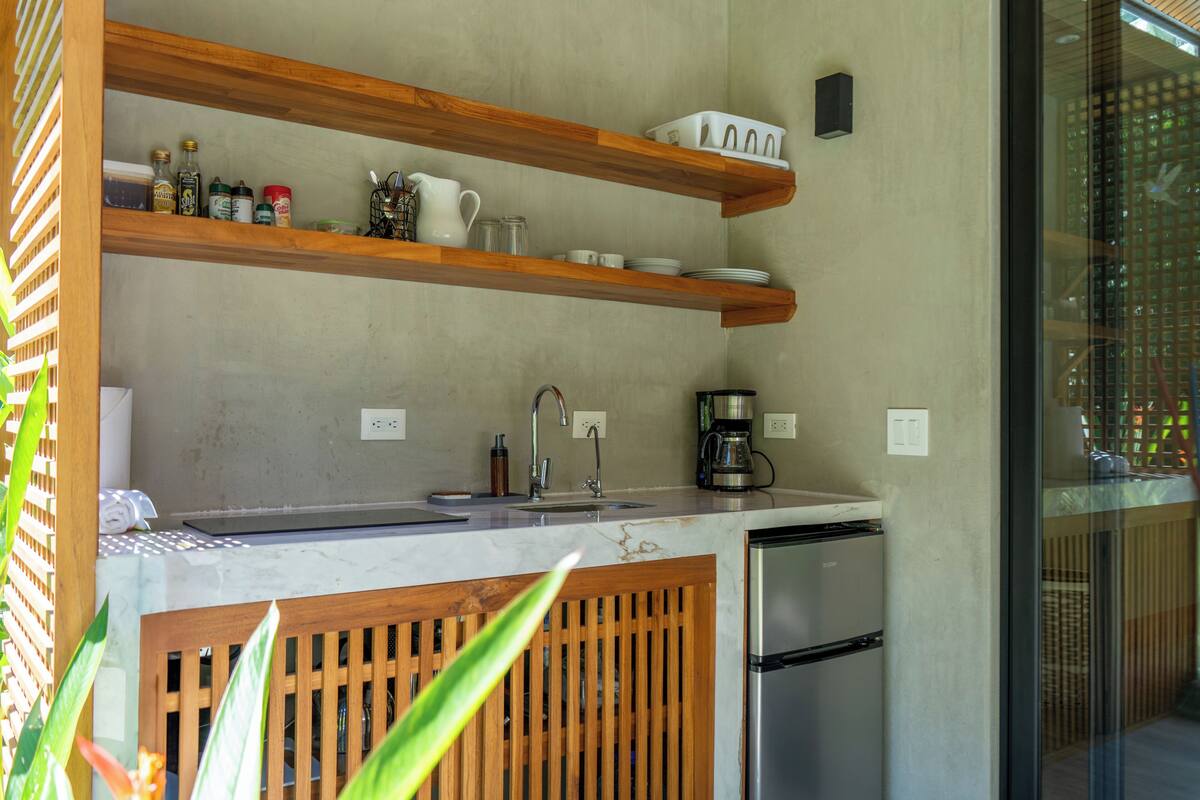 A modern kitchen with wooden shelves, a stainless steel refrigerator, and a marble countertop.
