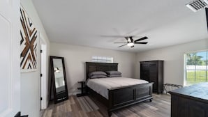 Une chambre à coucher avec un lit, un ventilateur de plafond, une armoire et un grand miroir.