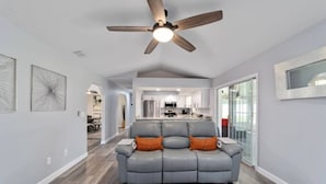 Un salon moderne avec un canapé en cuir gris, un ventilateur de plafond et un tapis à motifs géométriques.