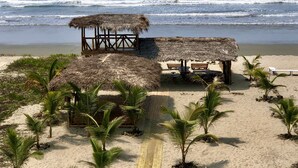 Una playa con estructuras de techo de paja, palmeras y un sendero arenoso que lleva al mar.