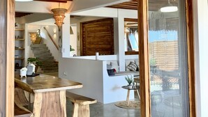 Una cocina moderna con vigas de madera, un comedor con mesa y bancos de madera, y lámparas colgantes de mimbre.