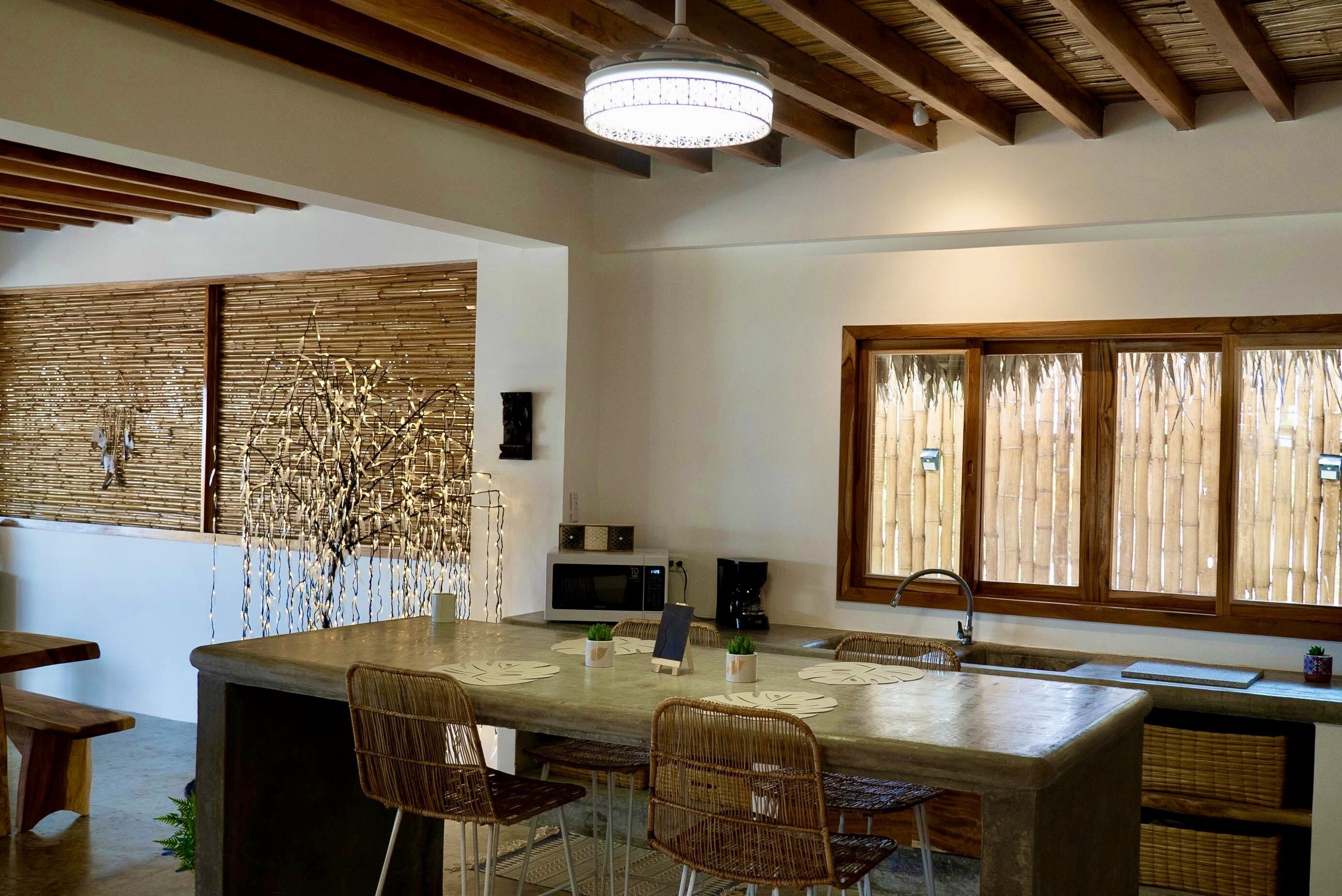 Una cocina moderna con una isla grande, vigas de madera en el techo y vistas a través de persianas de bambú.