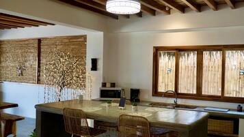 Una cocina moderna con una isla grande, vigas de madera en el techo y vistas a través de persianas de bambú.