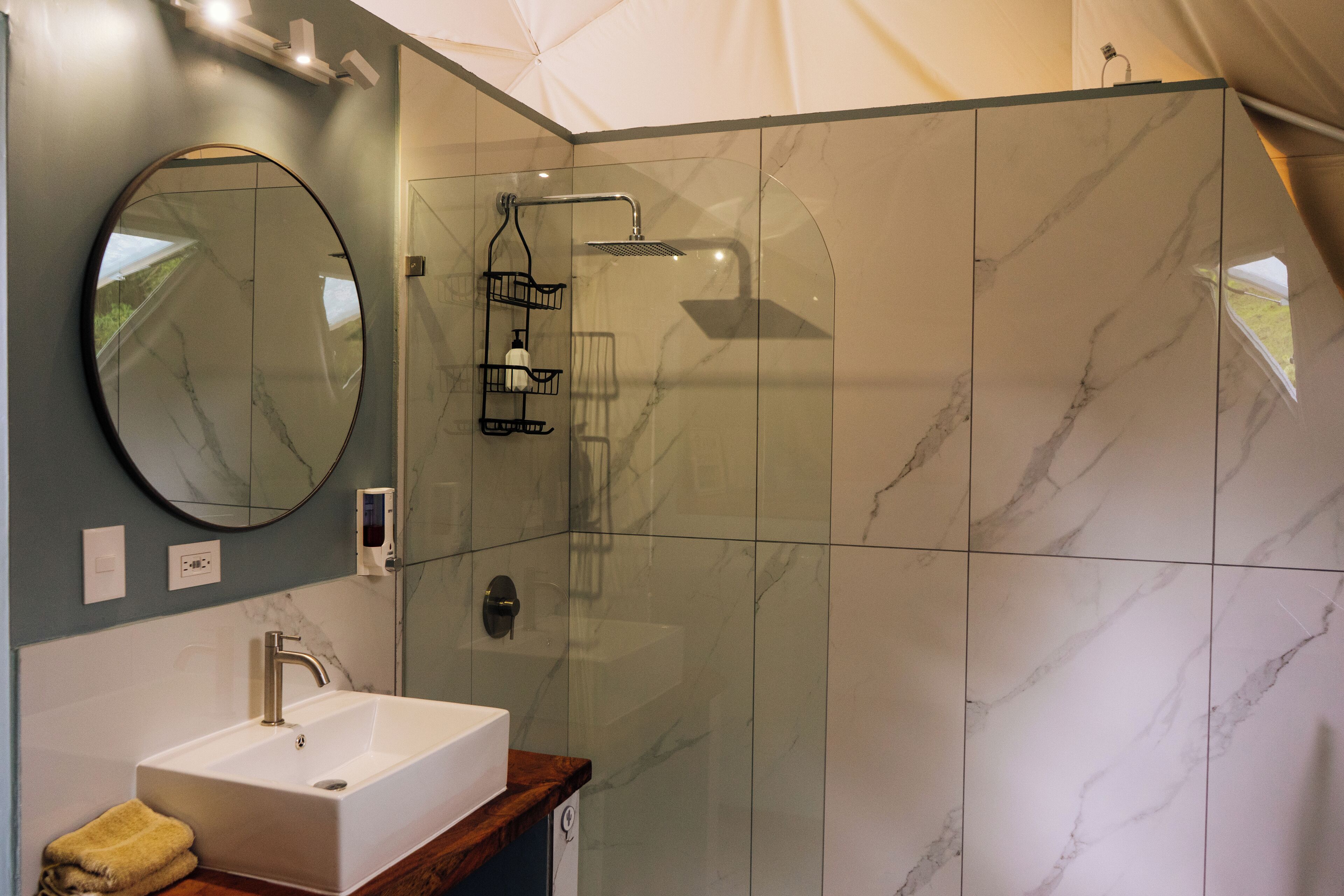 Un bagno moderno con doccia in marmo, lavabo con piano in legno e un grande specchio.