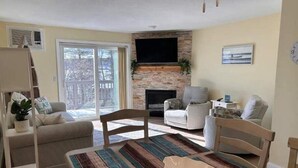 Una sala de estar con chimenea, un sofá, una mesa de comedor y un televisor montado en la pared.