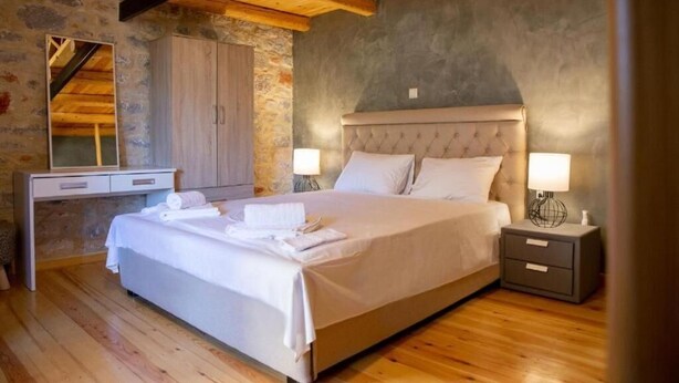 A bedroom with a large bed, wooden floor, stone wall, and a wooden ceiling. - Ximitadi Estate (East Mani)
