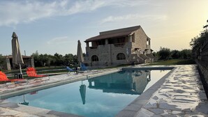A swimming pool with stone tiles, surrounded by lounge chairs and umbrellas, with a stone building in the background. - Ximitadi Estate (East Mani)