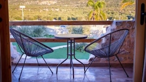 A balcony with two wireframe chairs and a small round table, overlooking a mountainous landscape with greenery and palm trees. - Ximitadi Estate (East Mani)