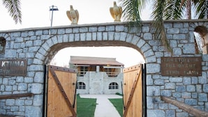 A stone archway with wooden gates leading to a building with a tiled roof. - Ximitadi Estate (East Mani)