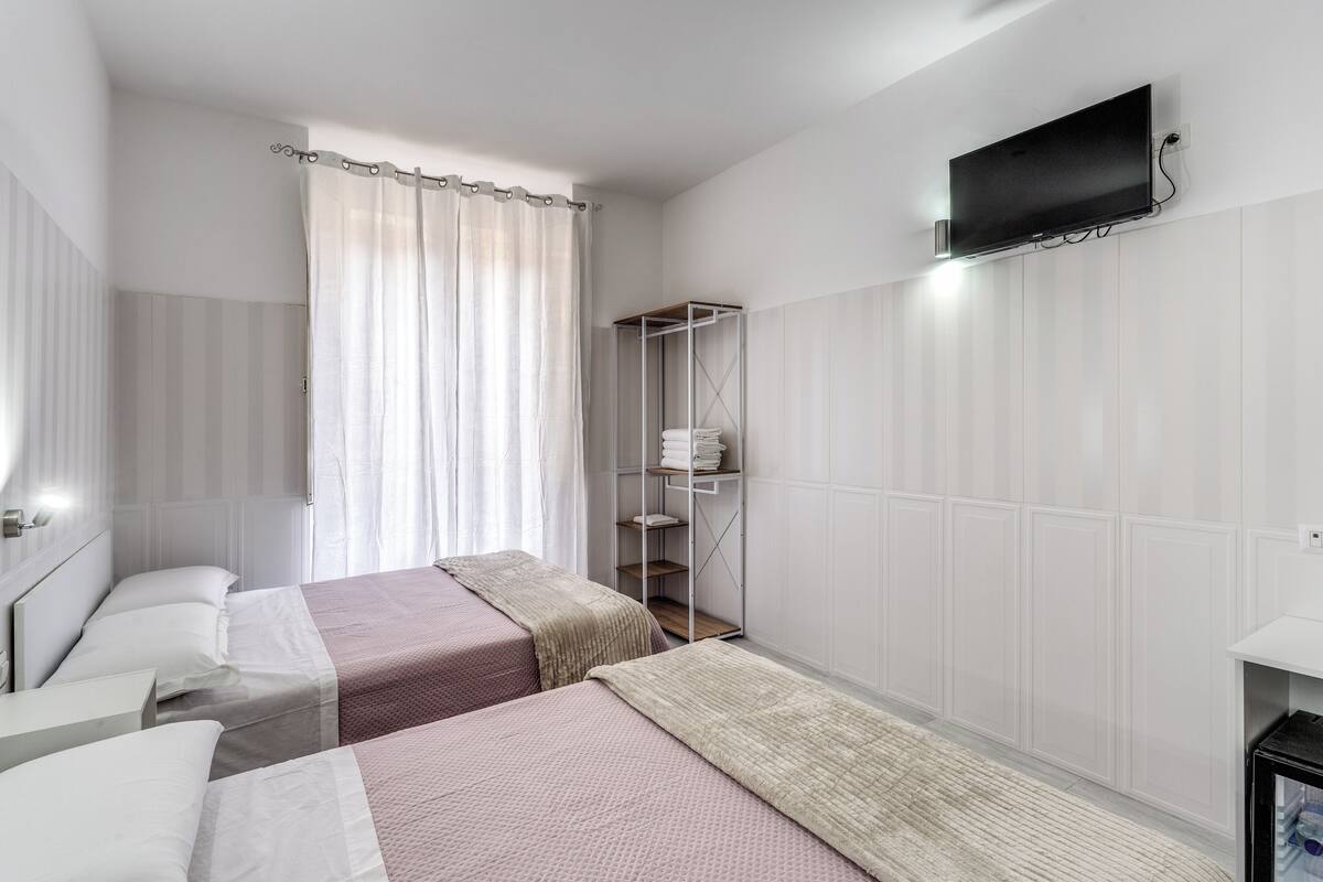 Habitación de hotel con dos camas, un televisor montado en la pared y un armario con repisas.