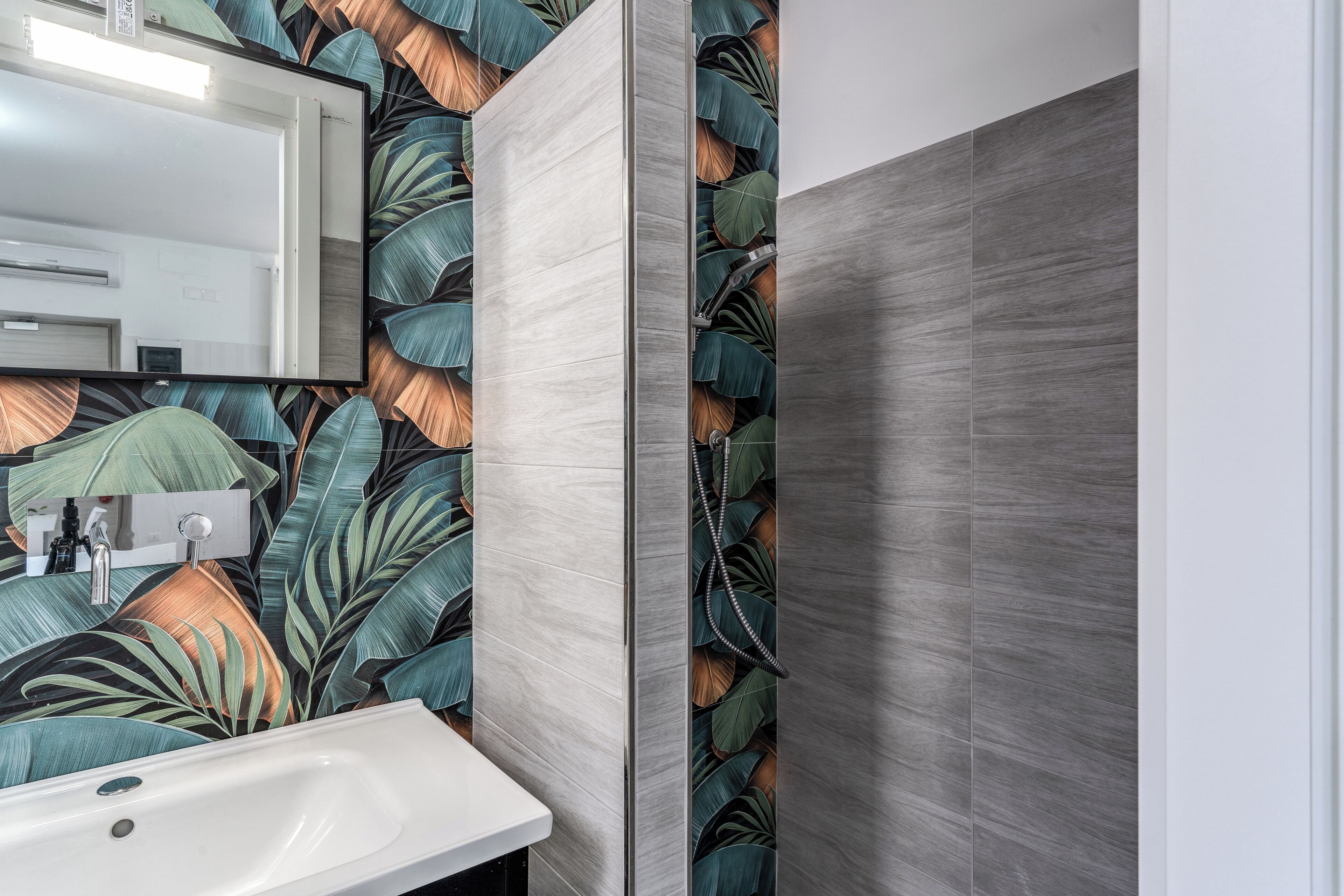 Une salle de bain avec un lavabo, un miroir et un mur orné d’un motif de feuilles tropicales.