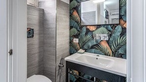 Une salle de bain au design moderne, dotée d’un grand miroir, d’un lavabo et d’un espace douche.