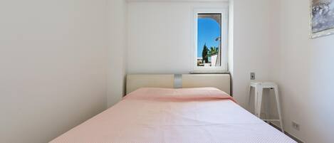 Un dormitorio con una cama individual, una ventana que da a zonas verdes y una escalera blanca adosada a la pared.