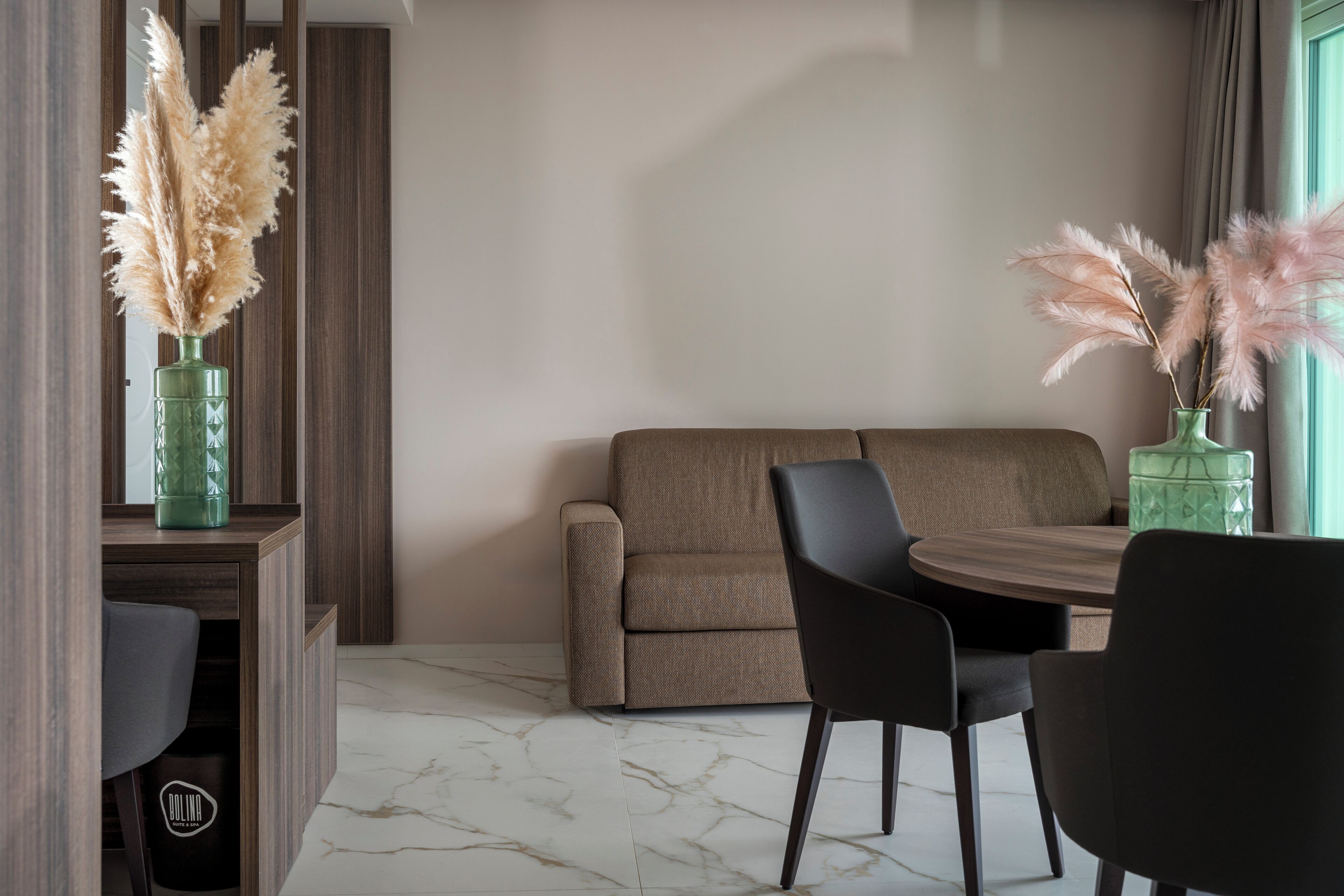 Een moderne woonkamer met een bank, stoelen, een eettafel en decoratief pampasgras in groene vazen.