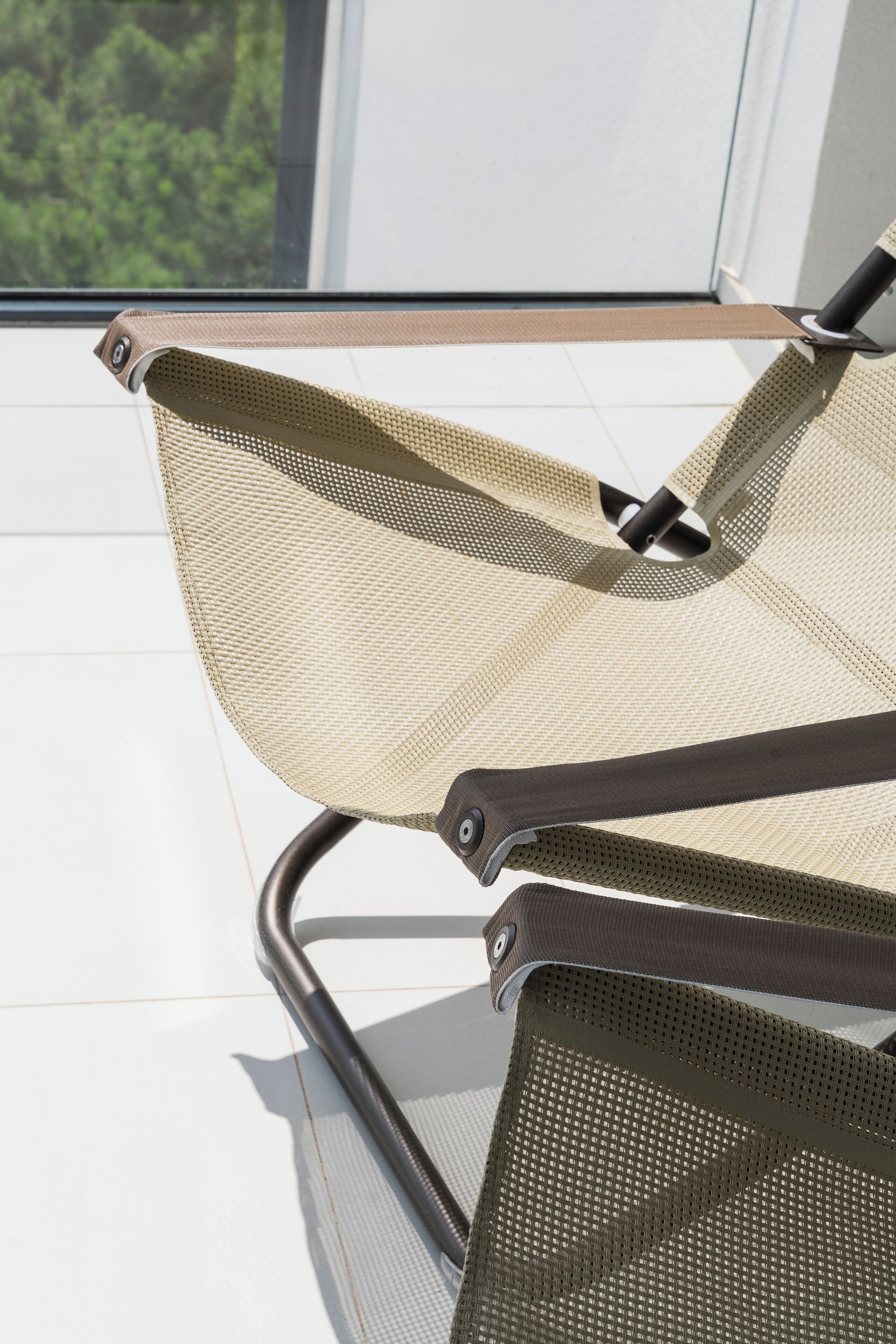 A chair with a mesh backrest and metal frame, positioned near a window with a view of greenery.
