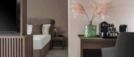 Une chambre d’hôtel avec un lit, une table de chevet, un bureau avec une caméra, un vase vert contenant des plumes d’herbe des pampas et une machine à café.