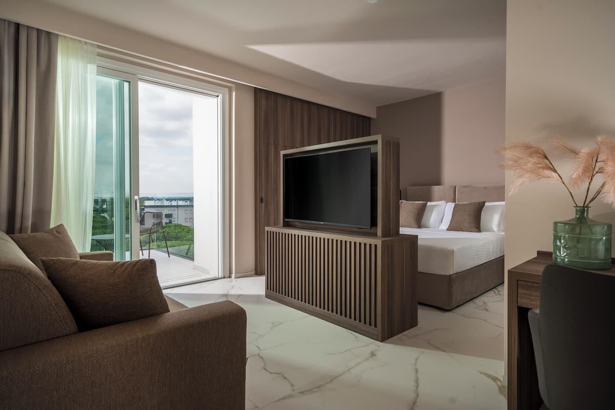 Ein modernes Hotelzimmer mit großem Fernseher, einem Bett, einer Couch und Blick auf die Stadt.