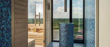 Une salle de bain moderne avec un plancher en bois, une colonne recouverte de carreaux bleus et une vue sur la campagne, visible à travers une grande fenêtre.