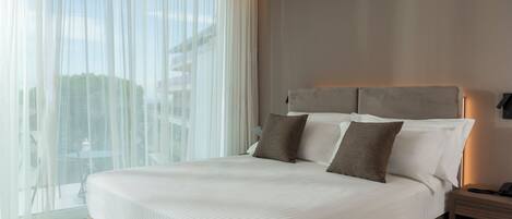 Una habitación de hotel moderna con una cama grande, una mesita de noche y vistas a través de cortinas traslúcidas.