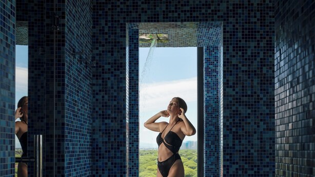 A woman in a black bikini standing in a tiled room with a view of greenery outside. - Bolina Suite Hotel (Cervia)