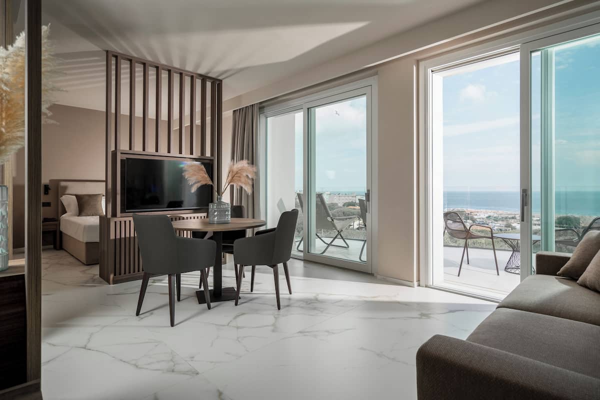 Ein modernes Wohnzimmer mit großem Fernseher, Essbereich und einem Balkon mit Aussicht.