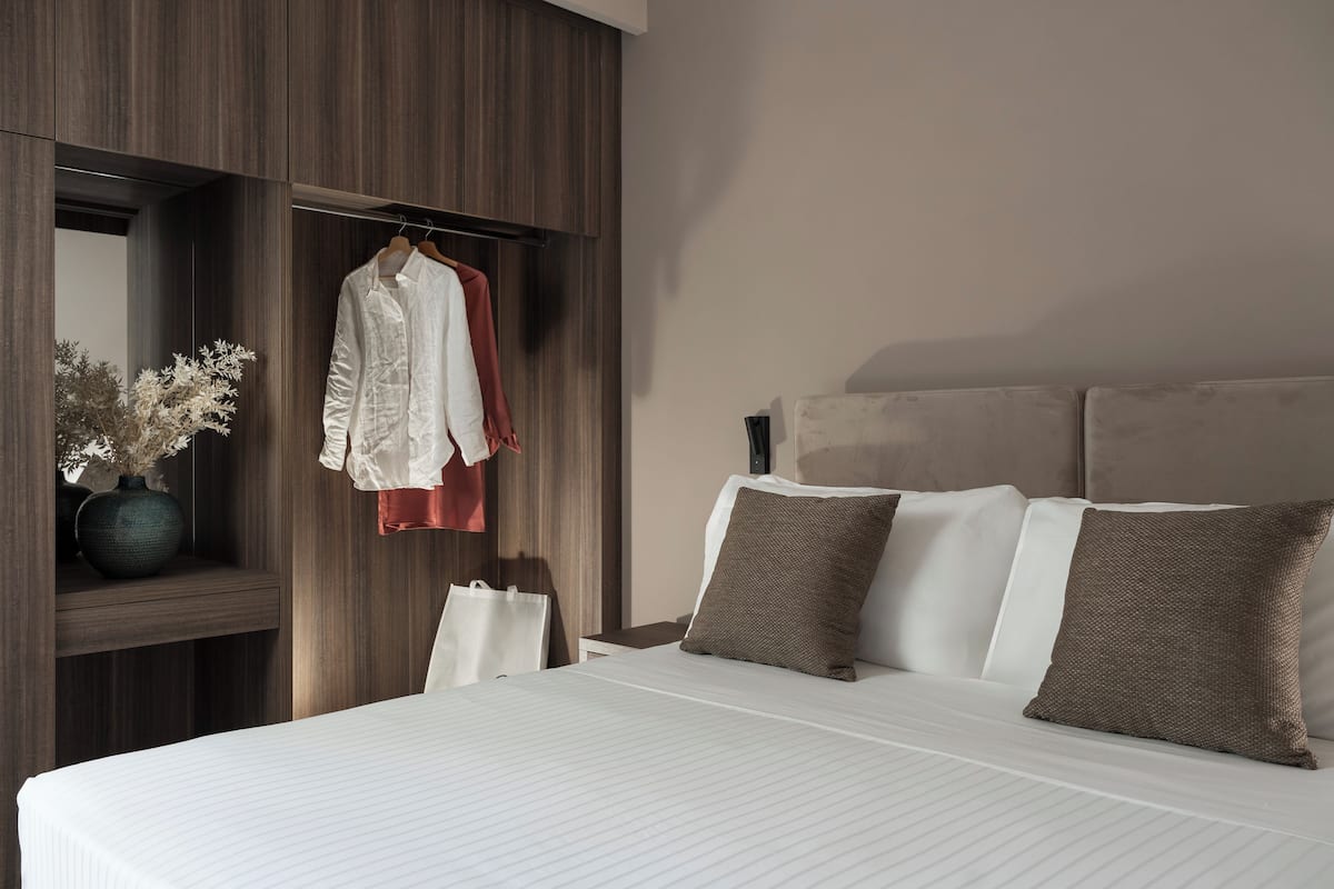 Ein modernes Hotelzimmer mit einem großen Bett, einem Holzschrank, einem aufhängbaren Bademantel und einer Vase mit getrockneten Blumen.