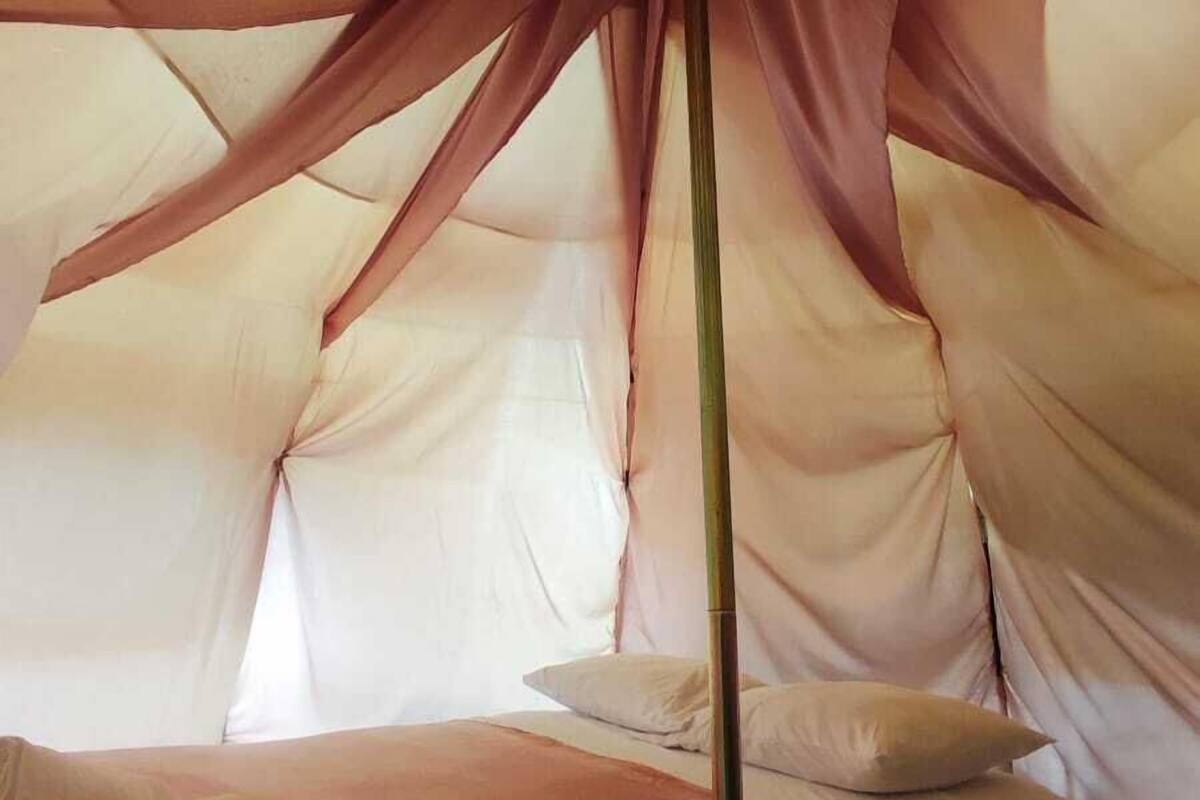 Une pièce en forme de tente, avec un lit, des oreillers et un poteau.